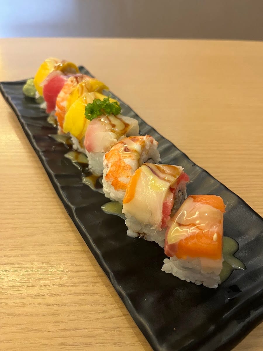 Rainbow sushi roll topped with salmon, tuna, prawn and mango on a long black plate