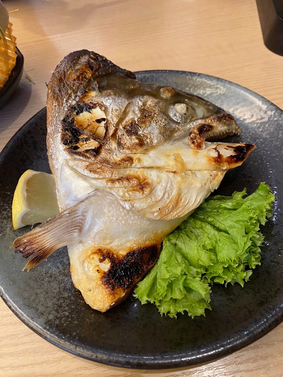 Grilled salmon head with lemon and lettuce on a dark plate