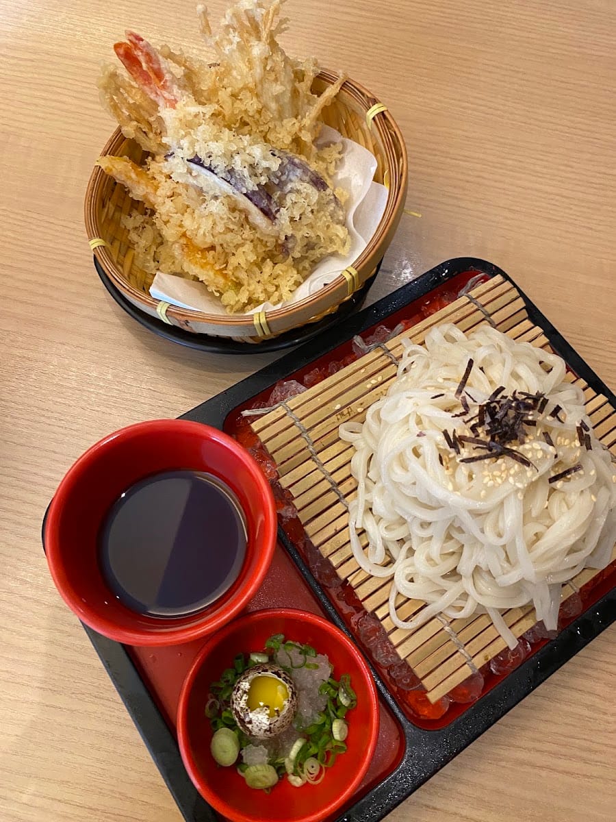 Tempura in a bamboo basket beside cold udon on a bamboo mat with dipping sauce